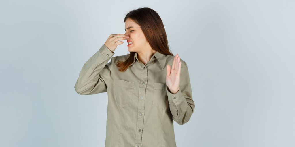 Woman holding her nose and making a disgusted face, reacting to a bad smell