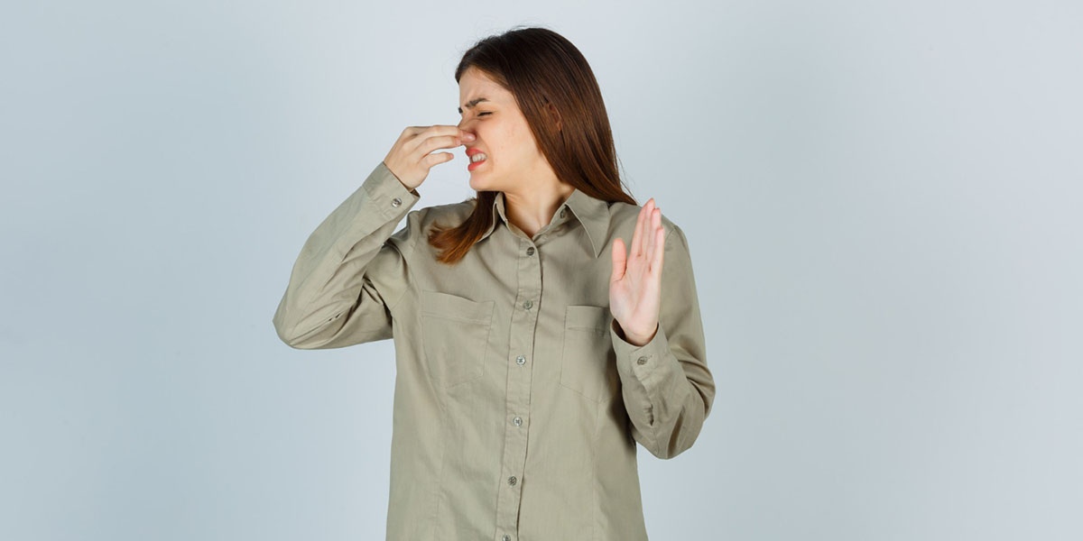 Woman holding her nose and making a disgusted face, reacting to a bad smell