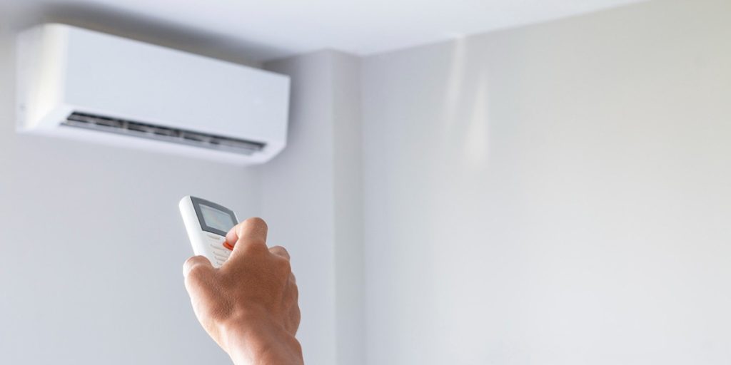 Person using a remote control to operate a wall-mounted air conditioning unit